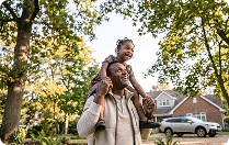 Man carrying a smiling child on his shoulders outdoors.